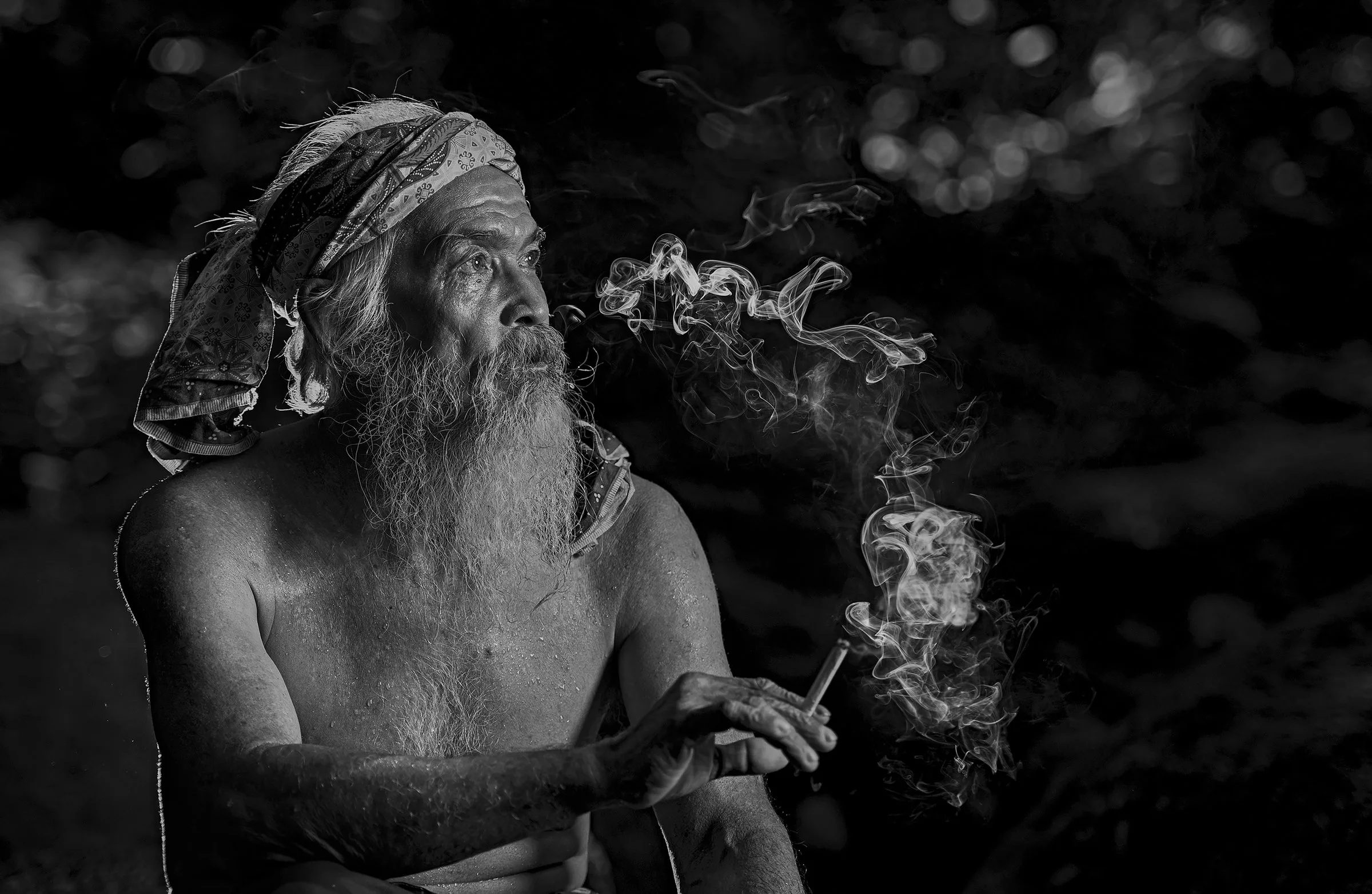 Black and white fine art portrait of an elderly bearded man exhaling smoke