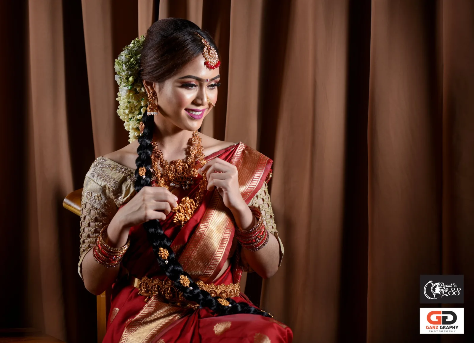 Smiling bride in a gold and brown saree holding her jasmine-decorated braid