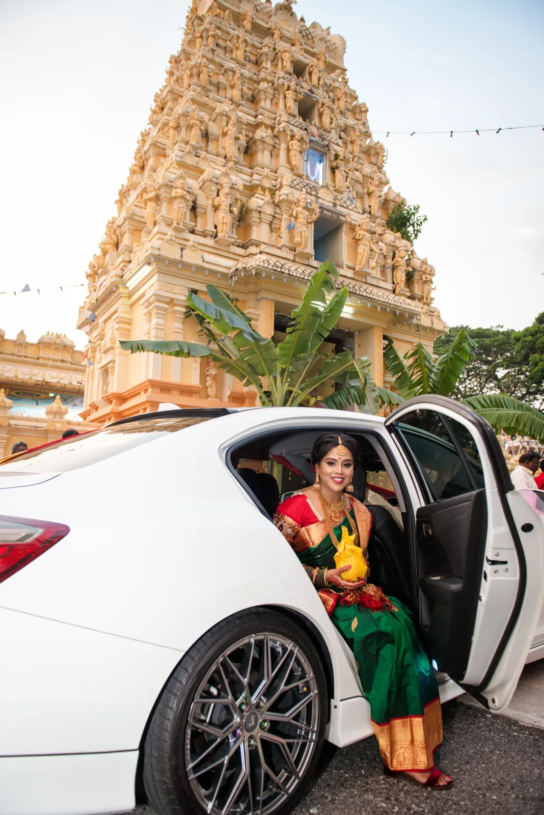Bride stepping out of a white car in front of a temple gopuram on her wedding day