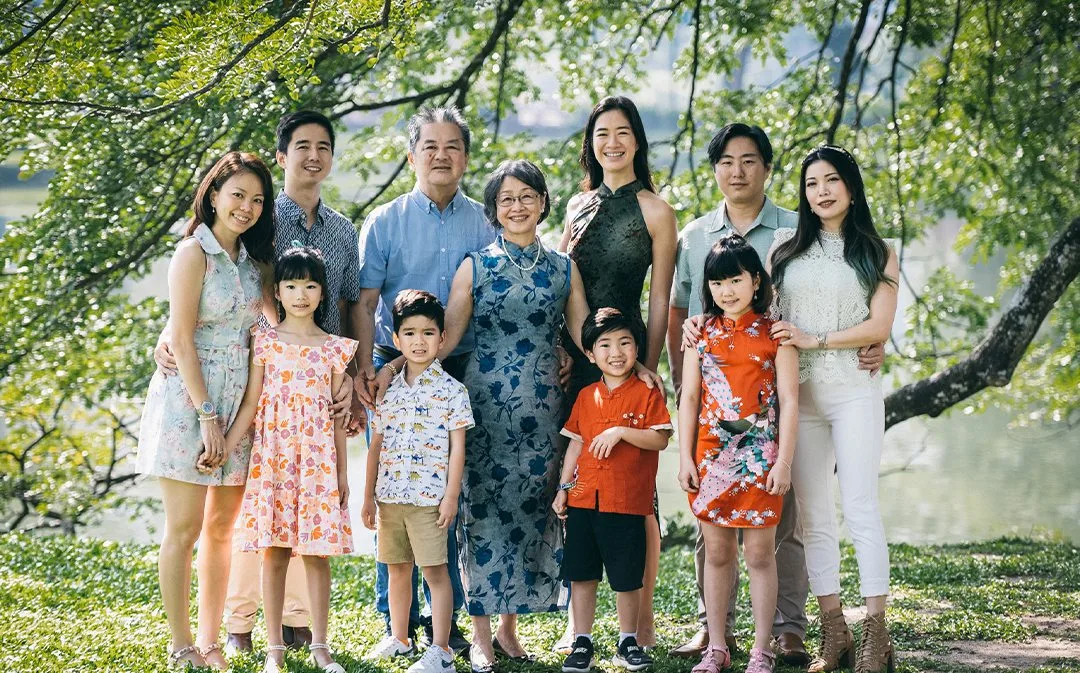 Large family portrait of three generations standing on the grass under green trees
