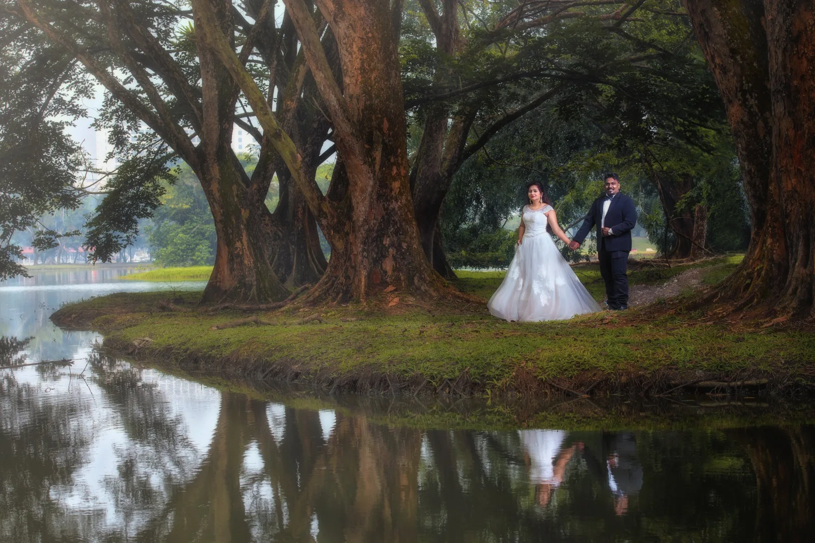 Couple holding hands under the rain trees of Taiping Lake Gardens with their reflection in the lake